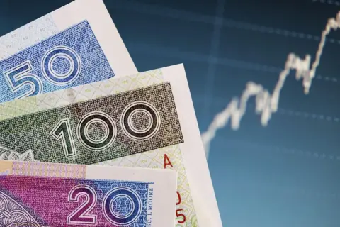 Polskie banknoty 20, 50 i 100 zł na tle wykresu giełdowego. Czy pieniądze w banku są bezpieczne?