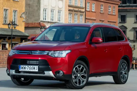 Czerwony Mitsubishi Outlander na tle kamienic. Wiele osób szuka mitsubishi outlander opinie, by podjąć decyzję o zakupie.