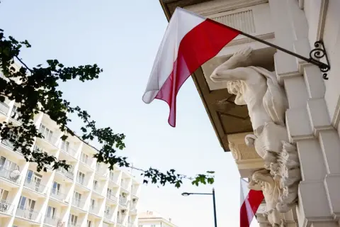 Biało-czerwona flaga powiewa na tle jasnego nieba, obok rzeźb atlantesów. Czy 2 maja jest wolny?