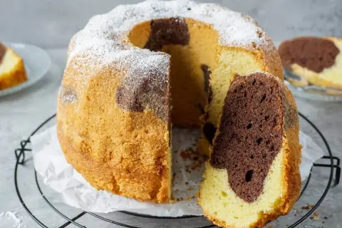 Ein saftiger Marmorkuchen, bestäubt mit Puderzucker, zeigt seine köstliche Maserung. Ein Stück wurde bereits entnommen, was ihn zum besten Marmorkuchen macht.