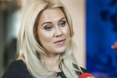 Caroline Hainer, med blont hår och makeup, ser åt sidan. En mikrofon syns i förgrunden.