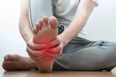 Persona che si tiene il piede, con un'area rossa che indica dolore sotto pianta del piede al centro.