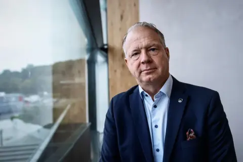 VD Volvo, en man i mörk kostym med Volvo-märke på kavajslaget, tittar mot kameran.