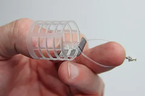 Ein Finger hält einen selbstgebauten Futterkorb mit Blei und Schnur.