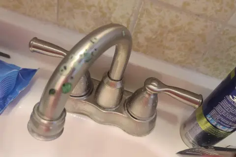 Rubinetti del bagno con calcare verde incrostato. Accanto, salviettine e una bomboletta di schiuma da barba.