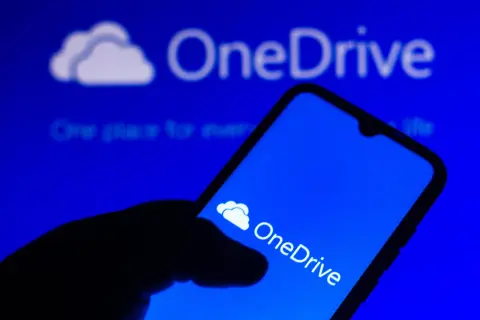 Dłoń trzyma smartfon z ikoną OneDrive. Szybki OneDrive download ułatwia dostęp do plików.
