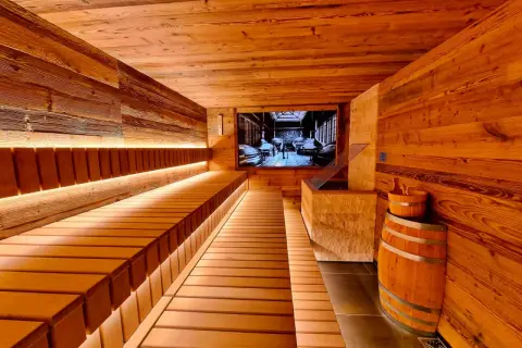 Gemütliche Holzsauna mit beleuchteten Bänken und einem Bild von einer Brauerei an der Wand. Ein Bierfass und ein Holzeimer stehen bereit für ein entspannendes Bier-Spa-Erlebnis.