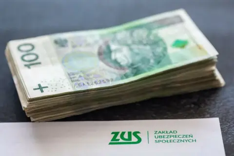 Stos banknotów 100 zł obok dokumentu ZUS. Może to symbolizować zarabianie na kontach bankowych lub oszczędzanie na przyszłość.
