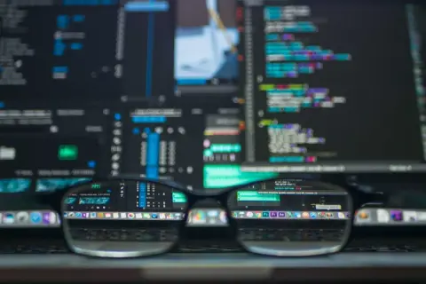 Okulary na tle ekranu z kodem. Programista analizuje kody PKD, tworząc nowe projekty.