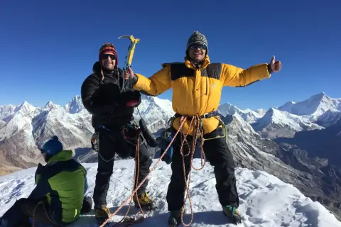 Dwóch alpinistów na szczycie Mera Peak, jeden z czekanem, drugi z kciukiem w górę. W tle ośnieżone góry.