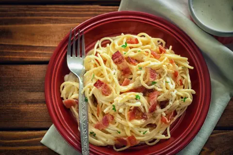 Pyszne spaghetti carbonara z chrupiącym boczkiem, posypane natką pietruszki. Idealne danie, gdy zastanawiasz się nad spaghetti carbonara kcal.