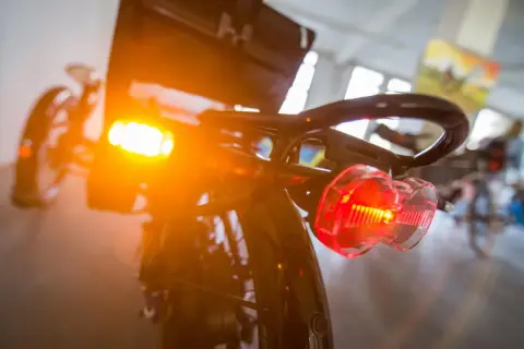 Blinker am Fahrrad leuchten orange und rot. Das Rücklicht ist klar erkennbar, während das vordere Licht diffus strahlt.