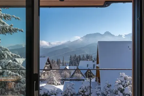 Zimowy krajobraz z ośnieżonymi domkami i lasem, idealny na nocleg z pięknym widokiem na Tatry.