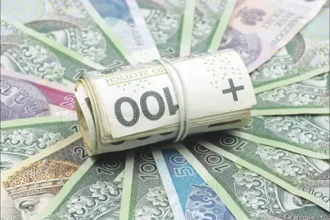 Zwijana rolka polskich banknotów 100 zł na tle innych banknotów.