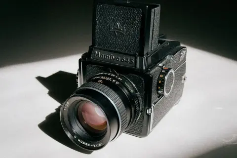 A classic Mamiya 645 medium format camera sits on a white surface, bathed in dramatic light and shadow.