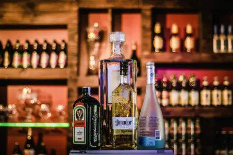 Butelki Jägermeister, El Jimador, Absolut i Hipnotiq na tle baru.