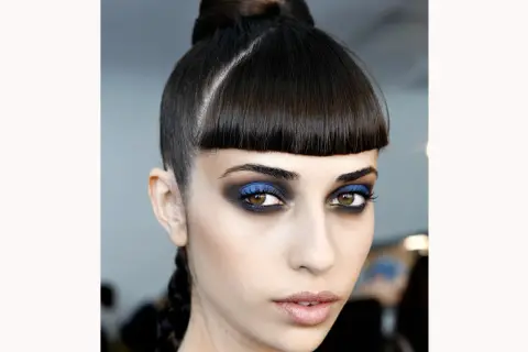 Occhi intensi con smokey eyes blu elettrico e nero, capelli raccolti in uno chignon e treccia.