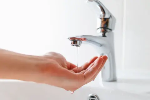 Main tenant, comment réduire la pression d'eau sur un robinet. Une main attrape un mince filet d'eau sortant d'un robinet moderne.
