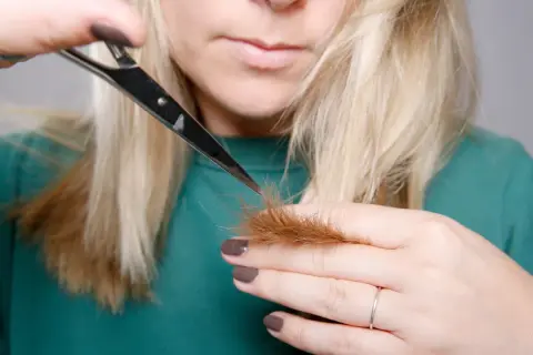 Kobieta z blond włosami uczy się, jak obciąć włosy, trzymając nożyczki przy końcówkach.