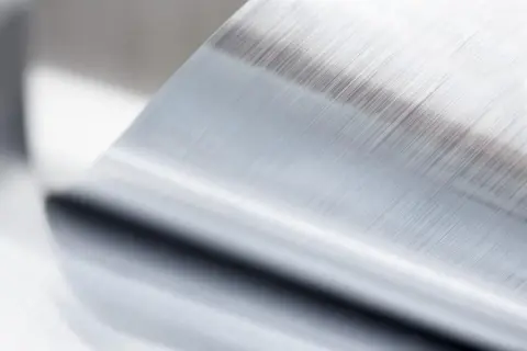 Szczotkowana powierzchnia metalu po procesie anodowania, z widocznymi równoległymi liniami.