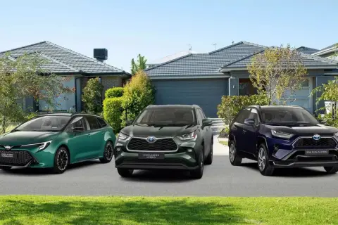 Trzy modele toyoty crossover: zielona Corolla Touring Sports, ciemnozielony Highlander Hybrid i granatowy RAV4 Plug-in Hybrid, stoją przed domami.