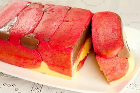 Zuppa inglese ricetta originale emiliana: strati di pan di spagna rosa, crema pasticcera gialla e cioccolato, decorata con savoiardi rossi e gocce di cioccolato.