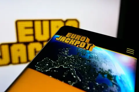 Logo Eurojackpot na ekranie telefonu z widokiem Europy nocą.