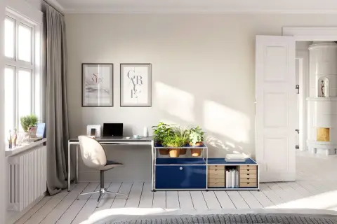 Accogliente stanza studio piccola con scrivania, piante e un'antica stufa in maiolica visibile attraverso una porta aperta.