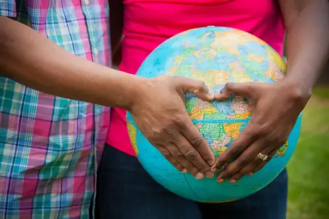 Mani a forma di cuore circondano un globo, simbolo del desiderio di adottare un bambino e accoglierlo nel mondo.