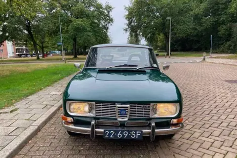En grön Saab 99 står parkerad på en tegelstensbelagd uppfart, redo för en tur genom svenska landskap.