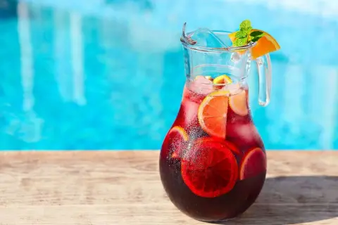 Pichet de sangria recette, rempli de fruits et de glaçons, prêt à être dégusté au bord de la piscine.