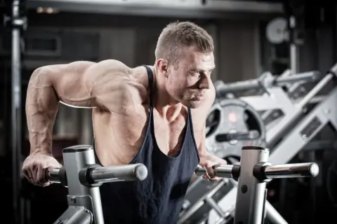 Mięśniowy mężczyzna wykonuje pompki na poręczach, jedno z najlepszych ćwiczeń na triceps.