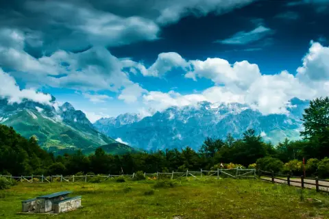 Majestuoso mirador de los Picos de Europa con nubes dramáticas sobre picos nevados y un prado verde.