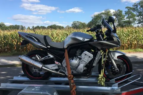 Srebrny motocykl Yamaha Fazer na przyczepce, gotowy do przerejestrowania. W tle pole kukurydzy i błękitne niebo.
