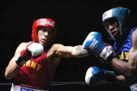 Two boxers, one in red with "ARMY" on his vest, the other in blue, engage in intense **sparring**. Their gloves are raised, ready for the next move in this practice bout.