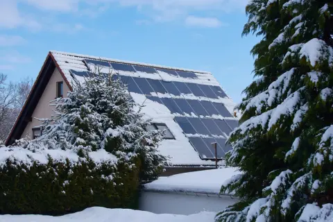 Schneebedeckte Solaranlage auf einem Hausdach, die zeigt, wie man im Winter heizen kann.