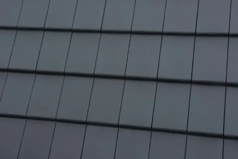 Zbliżenie na ciemnoszare dachówki ułożone w rzędy.