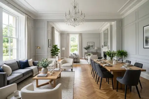 Elegancki salon w stylu angielskim z szarą sofą, drewnianym stołem i kryształowym żyrandolem.