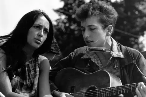 Młody Bob Dylan gra na gitarze i harmonijce, obok siedzi kobieta. To obraz z czasów, gdy jego twórczość zasłużyła na nagrodę Nobla.