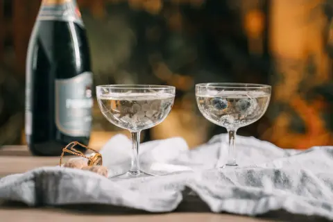 Dwa kieliszki z musującym winem, jeden z borówkami, obok butelka i korek. Czy wino musujące to szampan?
