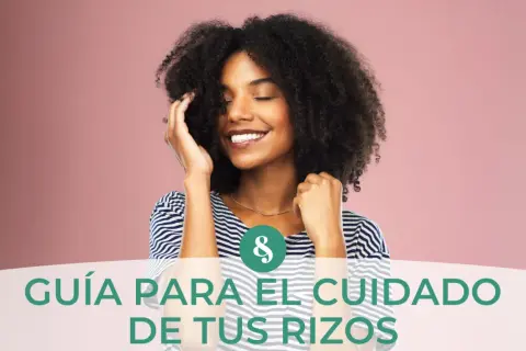 Mujer sonríe con ojos cerrados, tocando su pelo rizado. Guía para el cuidado de tus rizos, aprendiendo como hidratar el pelo rizado.