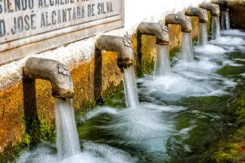 Fuente alta agua brota de varios grifos de metal, creando un riachuelo burbujeante.