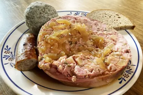 Saumagen-Rezept: Ein deftiger Saumagen mit Zwiebeln, Bratwurst und Brot auf einem Teller.