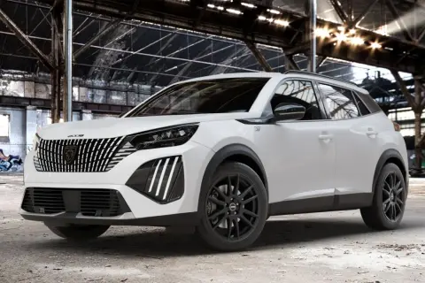 Biały Peugeot 2008 GT z czarnymi felgami stoi w opuszczonej hali przemysłowej, gdzie światło przebija się przez dach.