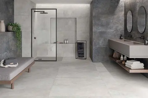 Baño moderno con ducha, lavabo doble y banco. Paredes y suelo revestidos con elegante material gres en tonos grises y oscuros.