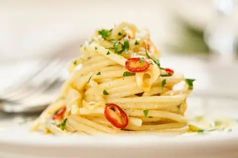 Ein Berg Spaghetti Aglio e Olio, garniert mit frischer Petersilie und scharfen Chilischeiben, auf einem Teller.