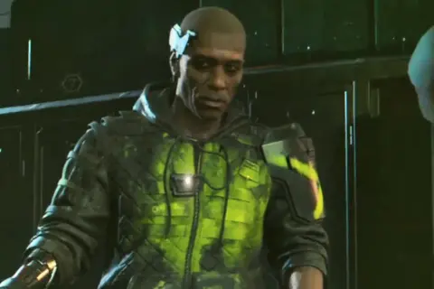 Mężczyzna w futurystycznej kurtce z neonowo-zielonymi wzorami. W tle ciemne, industrialne pomieszczenie. Nie czas żałować róż, to świat cyberpunk.