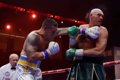 Boxer lands a punch as the referee watches. This intense moment captures the action, and in boxing, "UD" means a unanimous decision win.