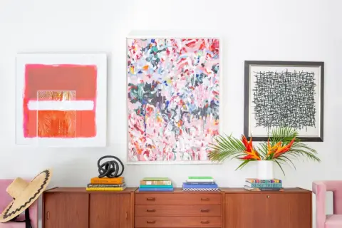 Vibrant abstract art and graphic prints adorn a wall above a midcentury credenza, showcasing a stylish blend of midcentury graphic design.