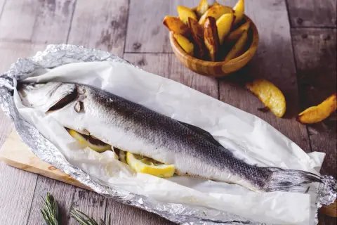Gegrillter Seebarsch mit Zitrone, bereit für den köstlichen Geschmack. Dazu knusprige Kartoffelspalten.